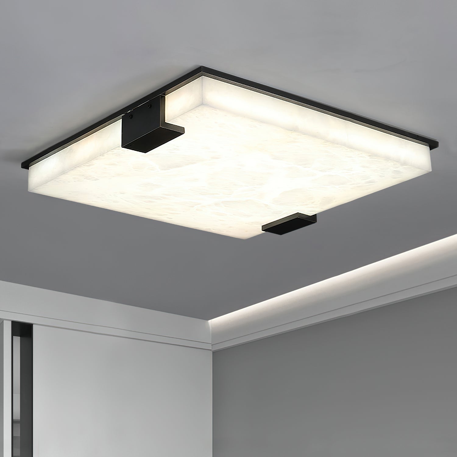 Clérachic ceiling light against a grey ceiling, its marbled alabaster surface lit edge to edge above a cove-lit wall.