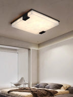 Clérachic flush mount in a bright bedroom corner, light pooling down the plaster wall beside sheer window blinds.
