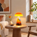 Lit Clérachic mushroom lamp on a round wood side table, beside a bud vase of orange flowers, books and a cream armchair.