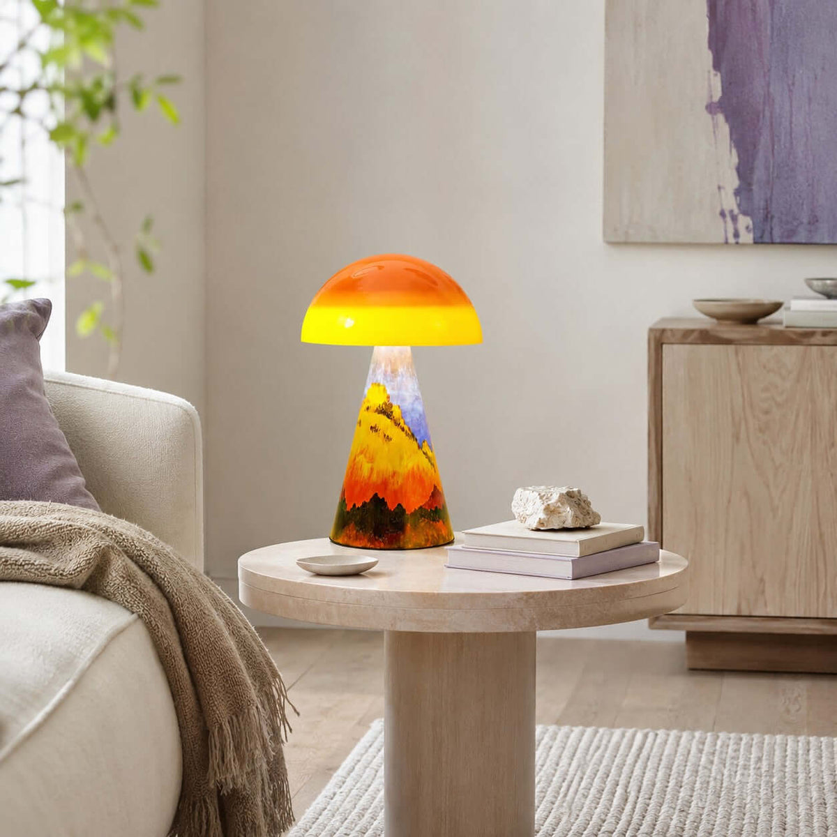 Clérachic mushroom lamp glowing on a pale round side table in a living room, with a stack of books and a stone ornament.