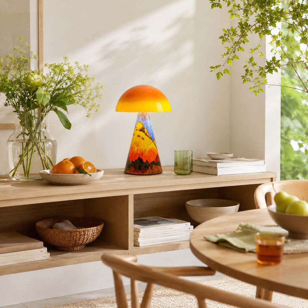 A Clérachic mushroom lamp on a low wooden shelf, with a bowl of oranges, a vase of green stems and a round table nearby.