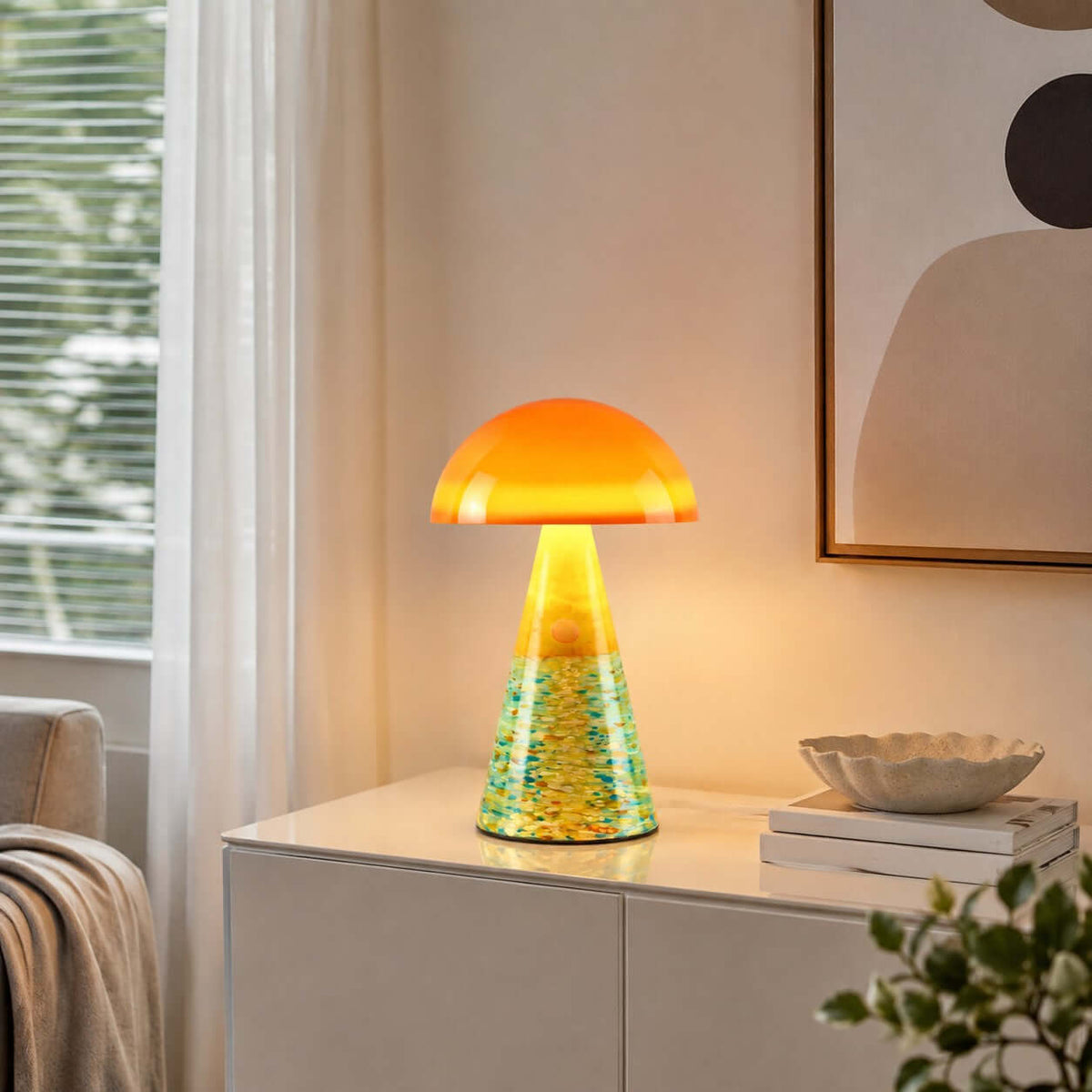 Sunrise Coast Clérachic table lamp lit on a white cabinet, with a green-and-yellow textured base and a shell-shaped dish beside it.