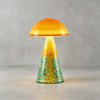 Close view of the Sunrise Coast Clérachic table lamp on a concrete floor, its teal and yellow painted cone glowing below an orange dome.