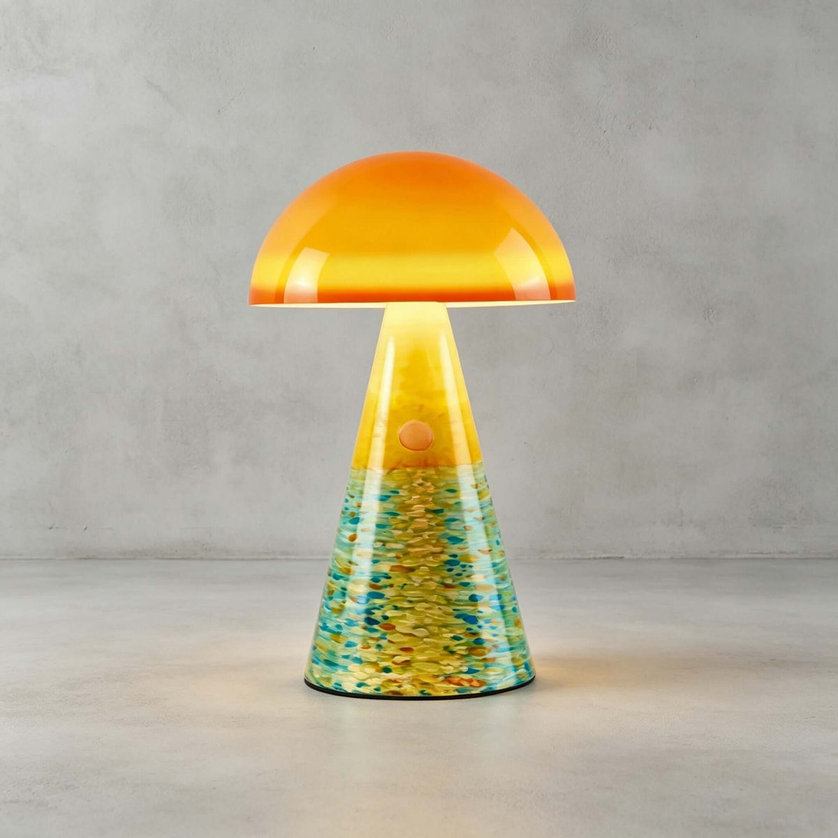 Close view of the Sunrise Coast Clérachic table lamp on a concrete floor, its teal and yellow painted cone glowing below an orange dome.