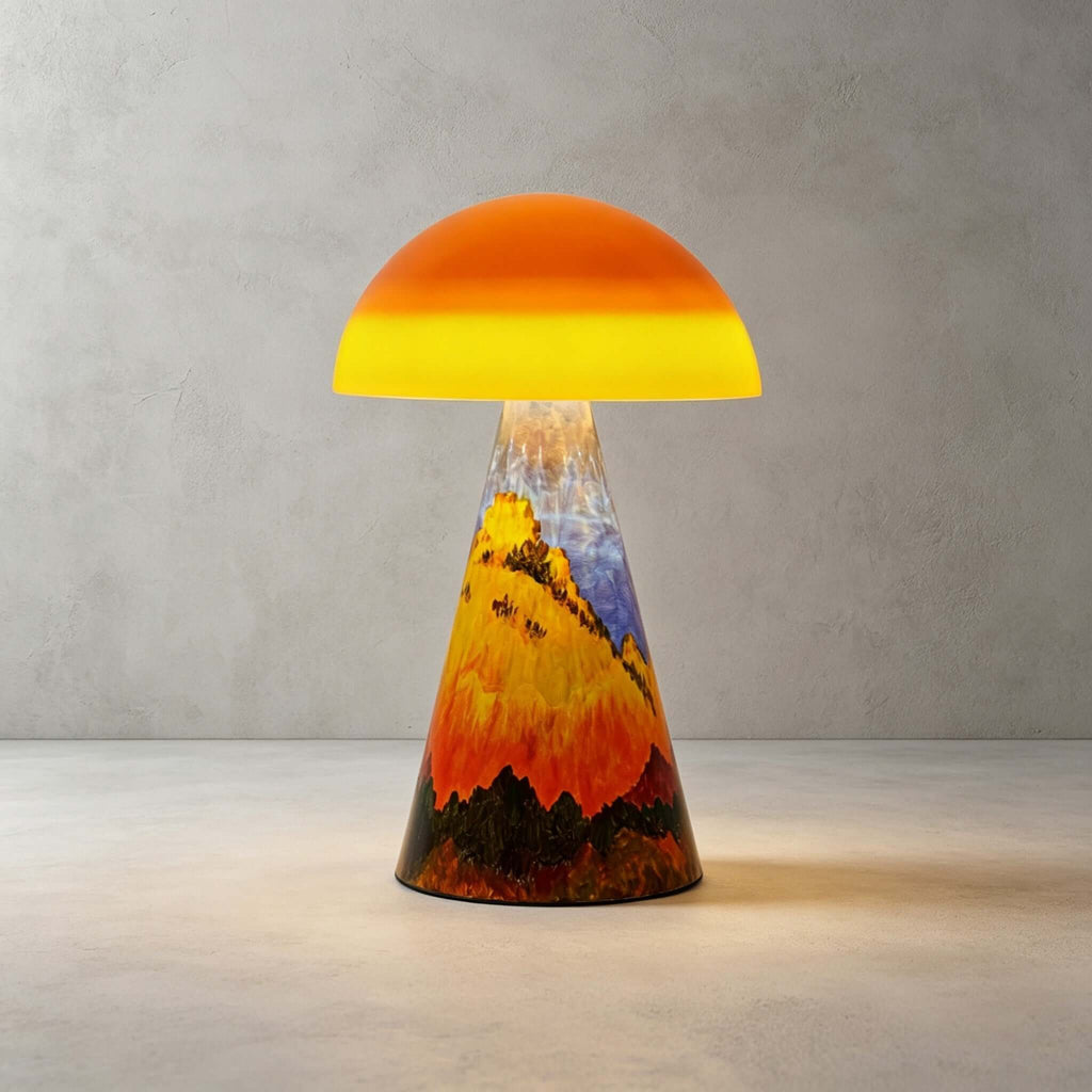 Close view of the Golden Peaks Clérachic table lamp on a concrete floor, with painted gold hills, red trees and a pale blue sky.
