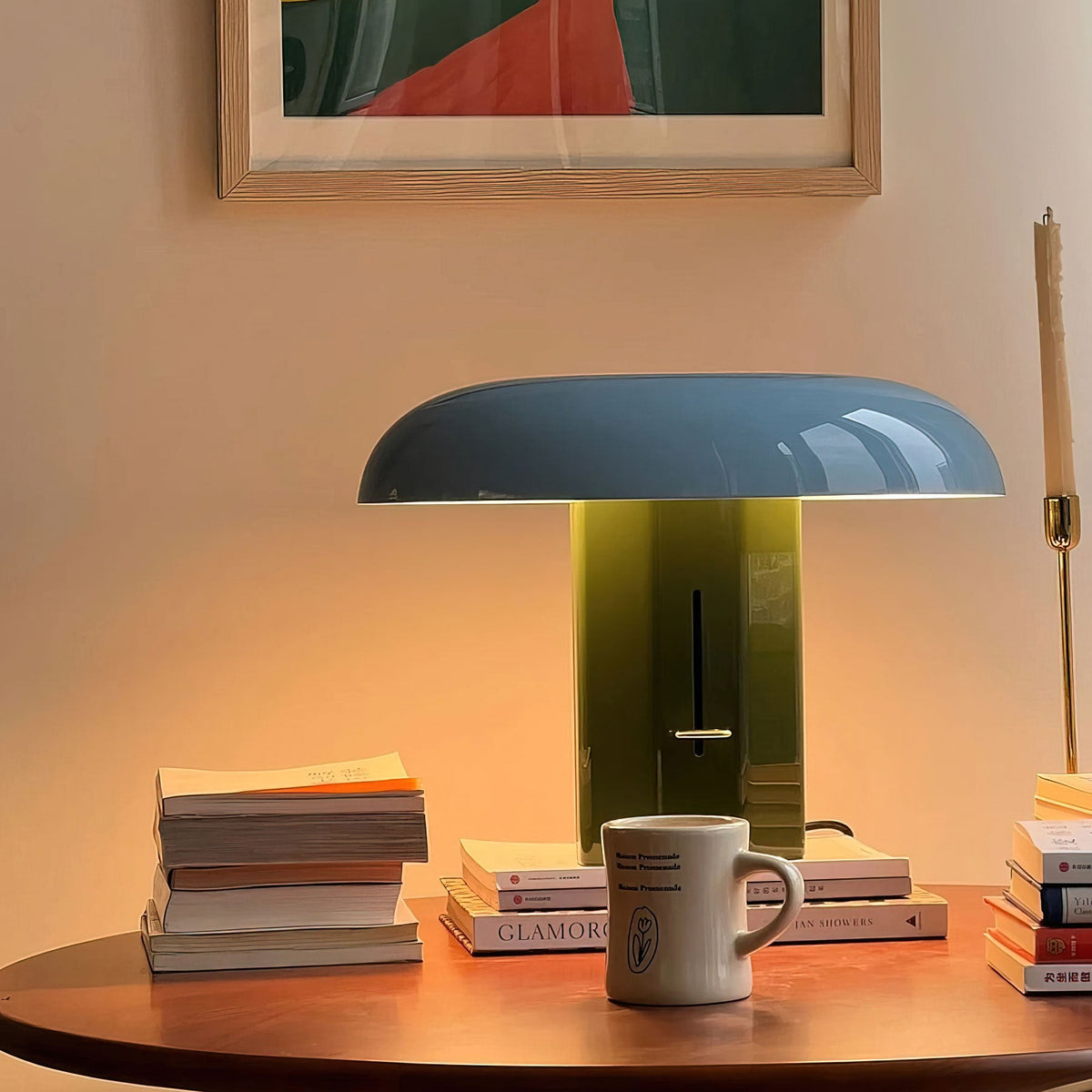 Warm light spills from this Clérachic table lamp with a blue shade and green base, standing beside a mug on a round wooden table.