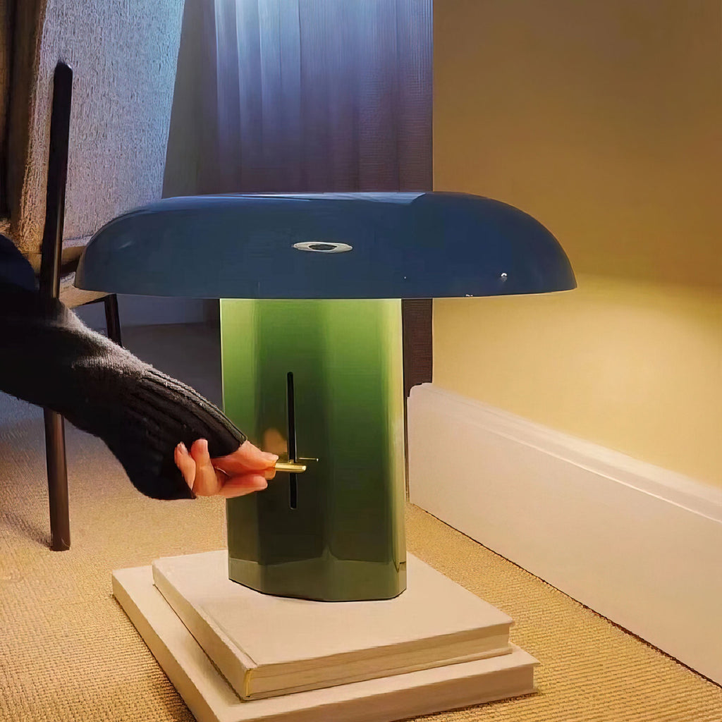 A hand reaches for the brass lever on the green column of this Clérachic table lamp, which sits on a stack of books.