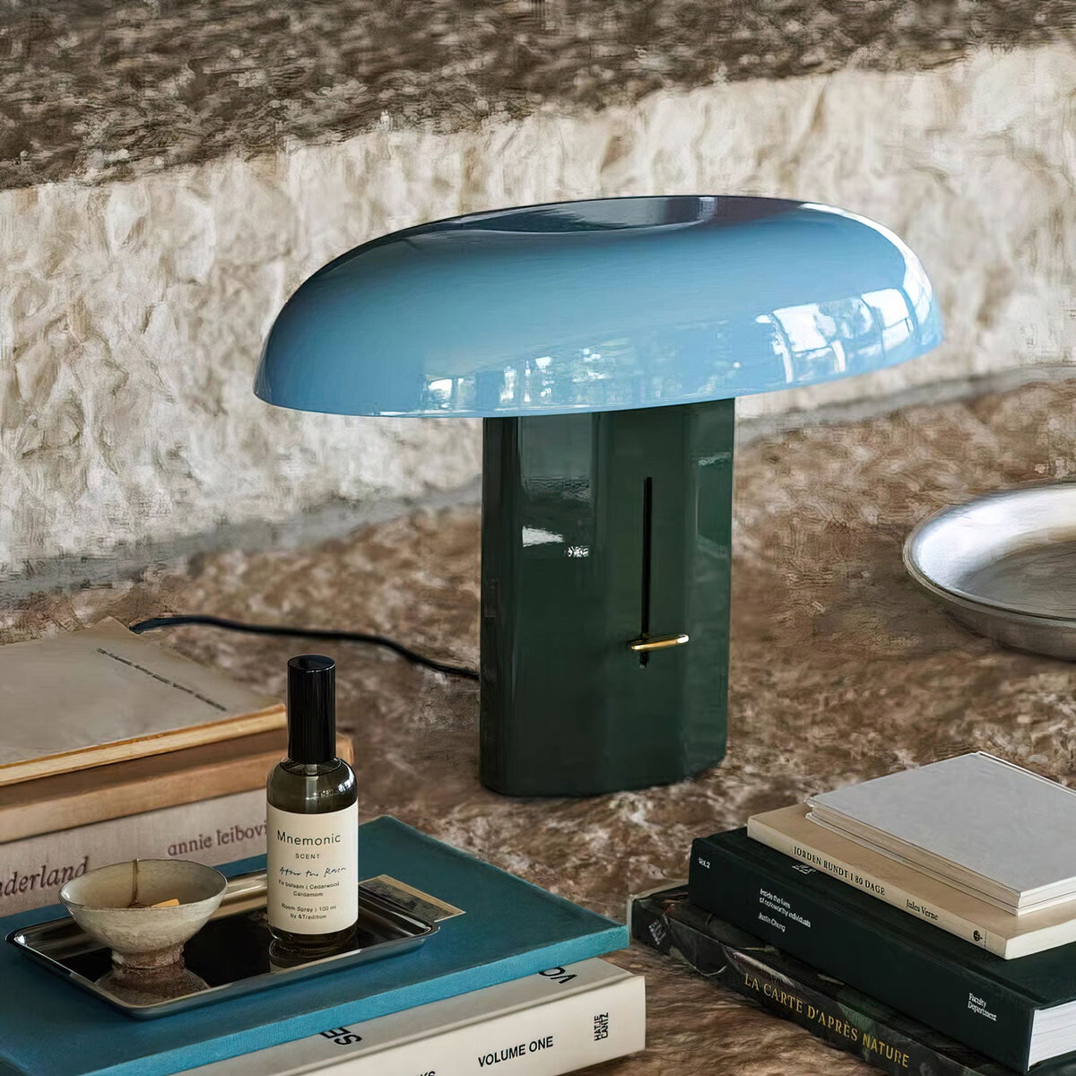Dark green base and pale blue shade on this Clérachic table lamp, with its black cord running across a stone surface.