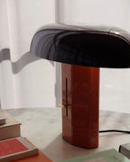 Glossy dark shade over a red-orange column on this Clérachic table lamp, beside books on a white marble top.