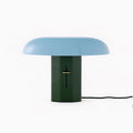 Front view of a Clérachic table lamp with a pale blue shade and green base, its black cord trailing to the right.