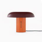 Front view of a Clérachic table lamp with a deep burgundy shade and orange base, its black cord trailing to the right.