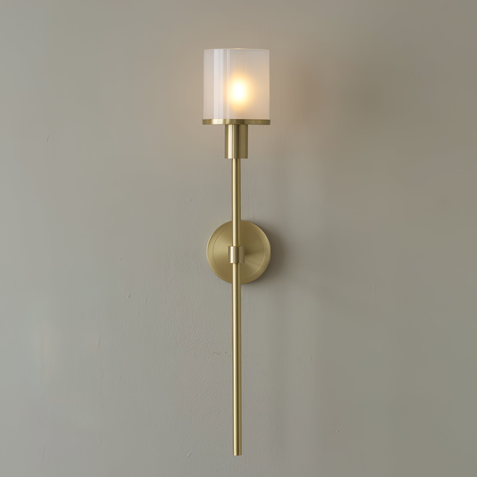 Clérachic Mycara wall sconce in copper, its fluted glass cylinder lit warm above a round backplate and slim stem.