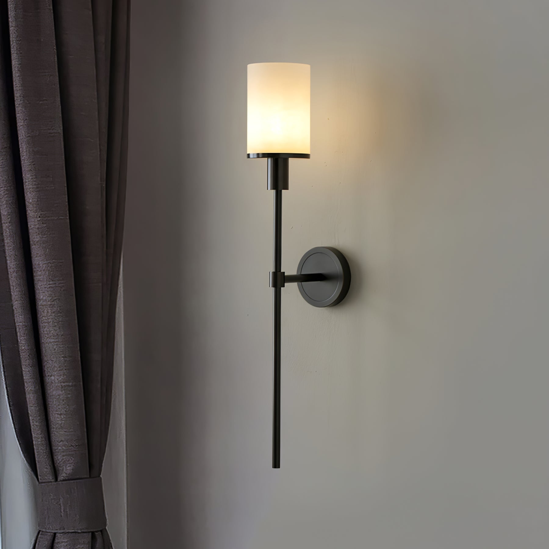 The Clérachic Mycara in black, mounted beside a pleated grey curtain with the glass shade glowing softly.