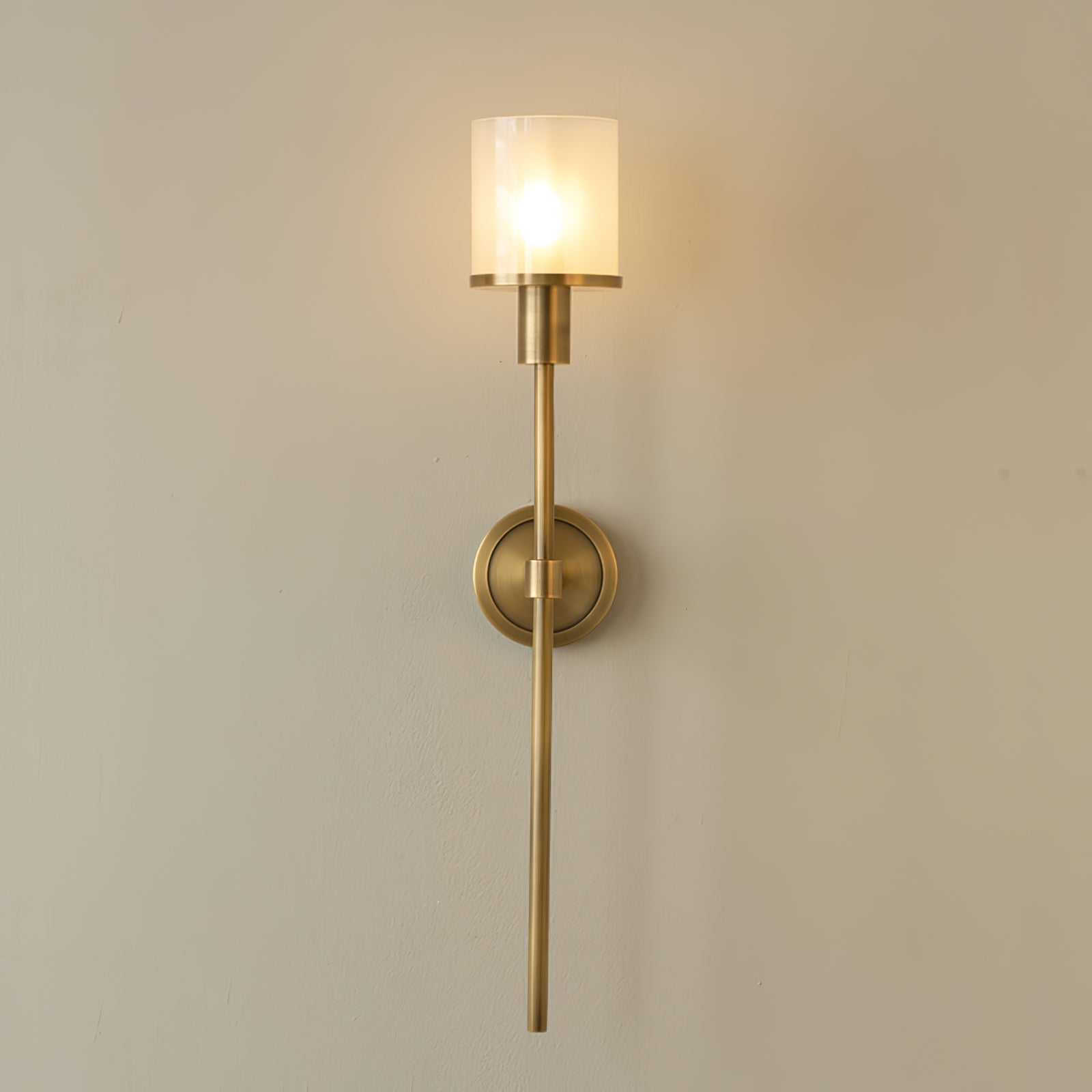 Clérachic Mycara sconce in polished copper, the lit glass shade casting a warm pool across a cream wall.