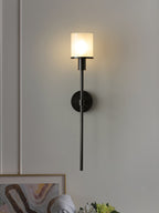 Clérachic Mycara in black, lit on a panelled wall above a leaning print and a vase of white blooms.