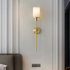 The Clérachic Mycara with its alabaster shade on a panelled bedroom wall, beside a grey upholstered seat.