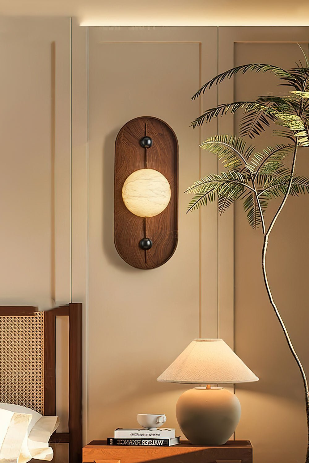 The Clérachic sconce glows beside a bed, next to a slim indoor palm and a ceramic table lamp on the side table.