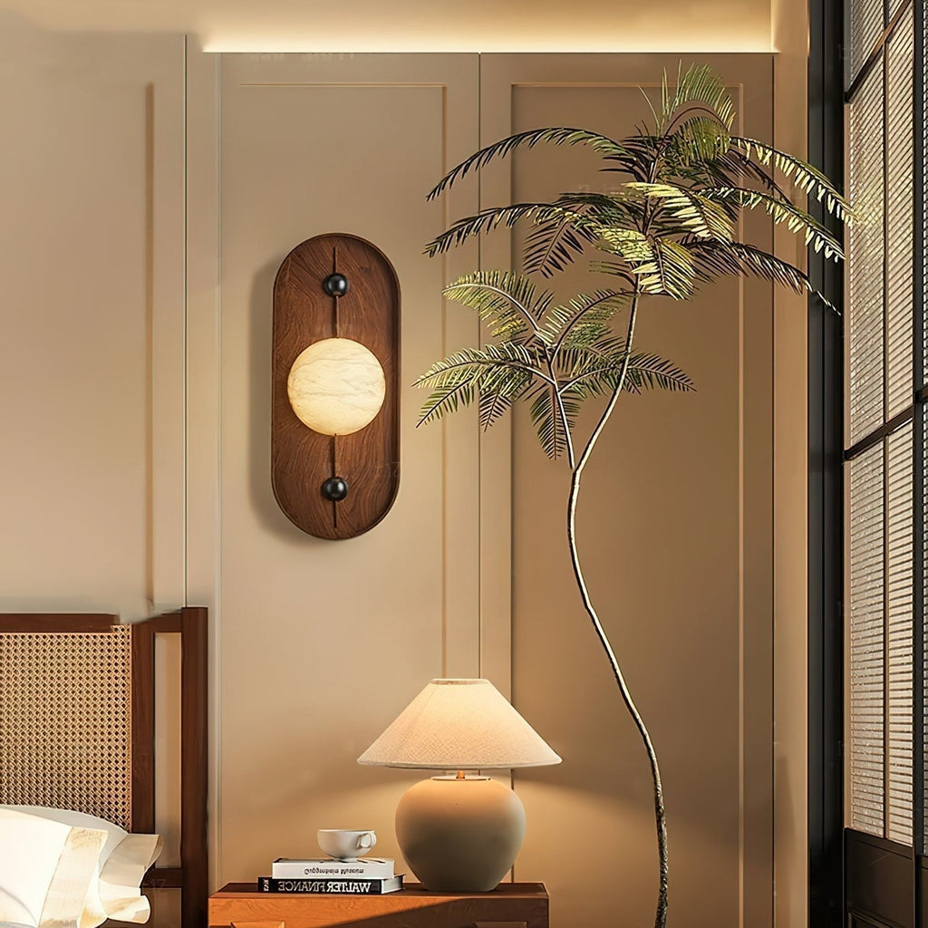 The Clérachic wall light warms a bedside corner, its glow meeting a dome table lamp and a tall palm frond.