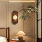 The Clérachic wall light warms a bedside corner, its glow meeting a dome table lamp and a tall palm frond.