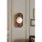 Clérachic hangs the oval sconce beside panelled doors with slim brass handles, framed art catching the spill of light.