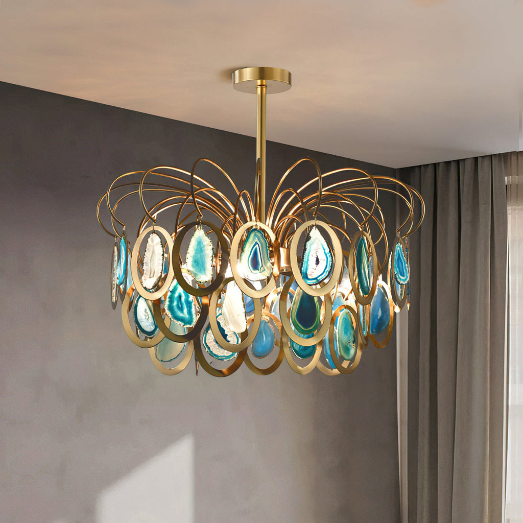 A blue Clérachic agate chandelier hanging against a grey plaster wall with a curtain at the side, its brass loops catching the light.