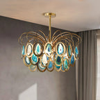 A blue Clérachic agate chandelier hanging against a grey plaster wall with a curtain at the side, its brass loops catching the light.