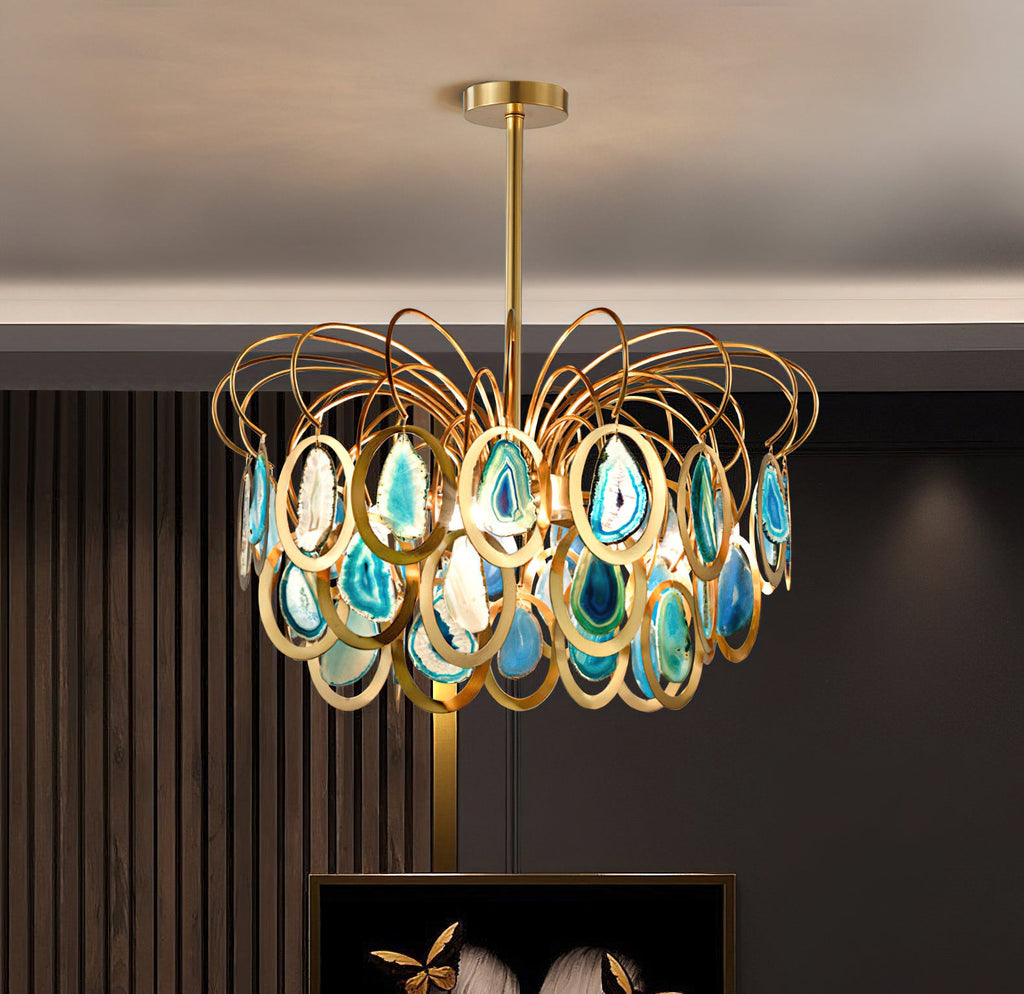 A Clérachic chandelier in blue agate and gold hung before a dark slatted wall, with a framed picture just visible below.