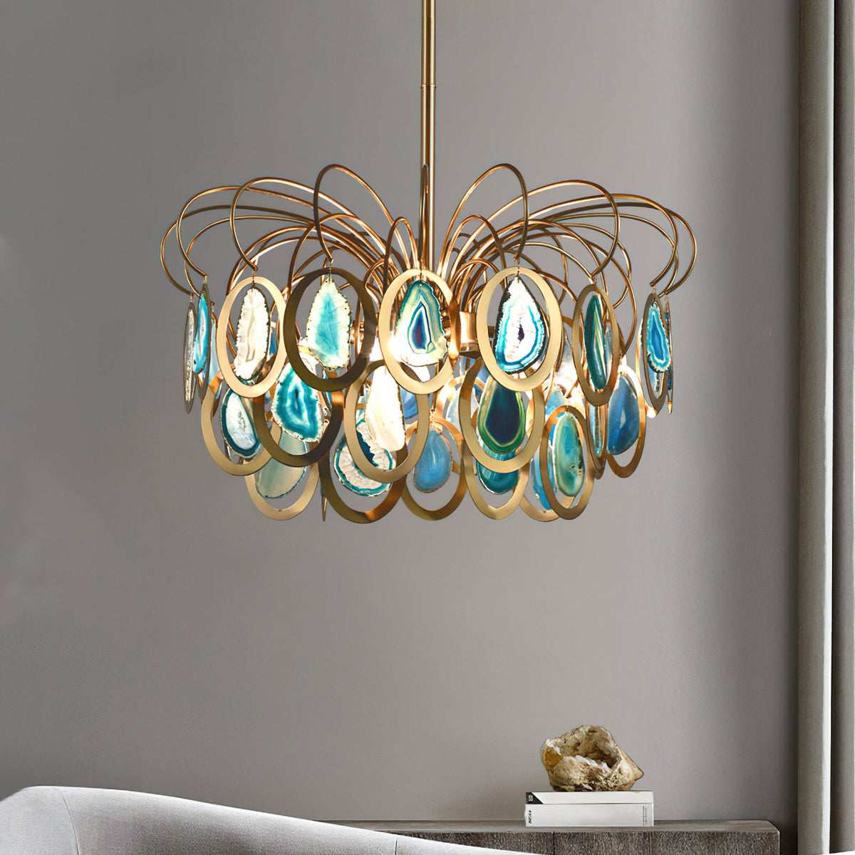 Clérachic blue agate chandelier on a long gold stem against a grey wall, with a small ornament on a console beneath it.