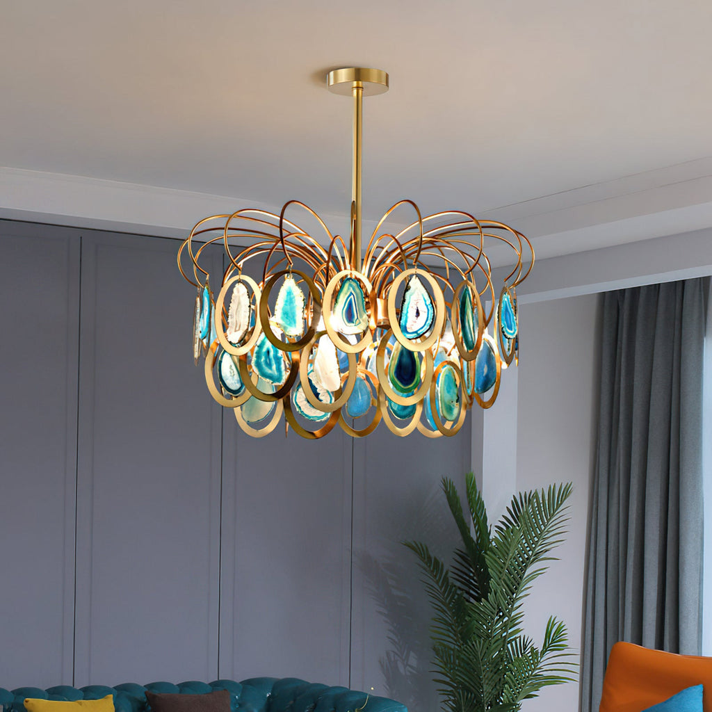A Clérachic blue agate chandelier in a grey-panelled room with a tall green plant and a teal sofa at the edge of the frame.