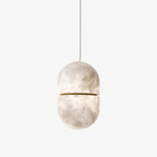 A Clérachic capsule pendant in veined natural alabaster on a plain light backdrop, split by a slim gold band and hung from a thin white cord.