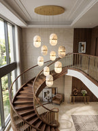 Seen from above, a cascade of Clérachic alabaster pendants hung from a round gold canopy beside a spiral staircase and tall windows.