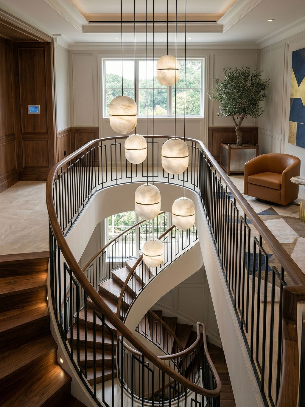 A cluster of Clérachic alabaster pendants at varied heights over a stairwell with a black railing and a leather armchair beyond.