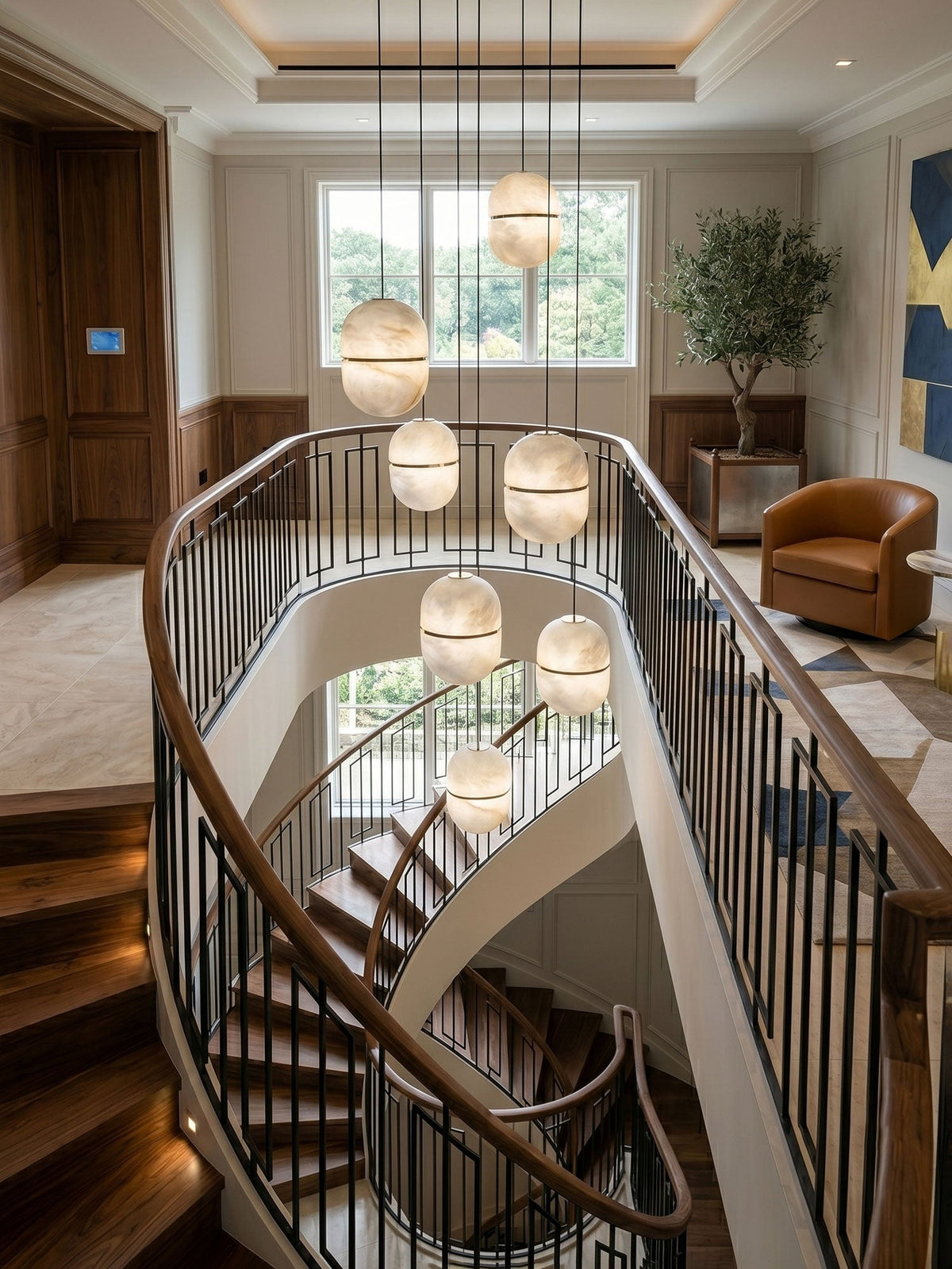 A cluster of Clérachic alabaster pendants at varied heights over a stairwell with a black railing and a leather armchair beyond.