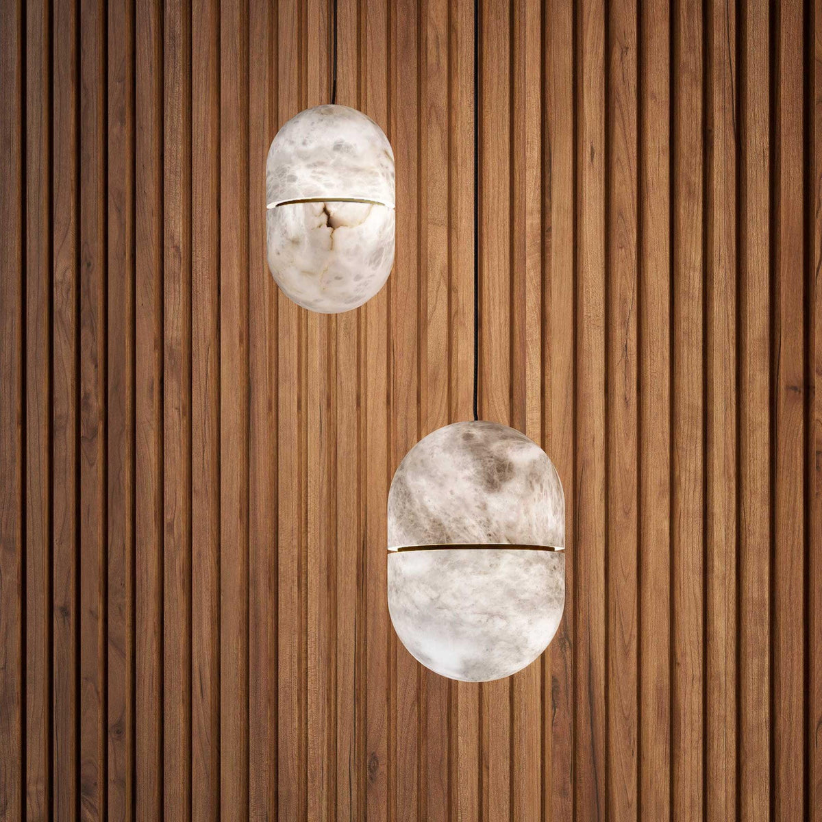 Two Clérachic alabaster pendants at different heights against a wall of warm timber slats, each with a thin band at the middle.
