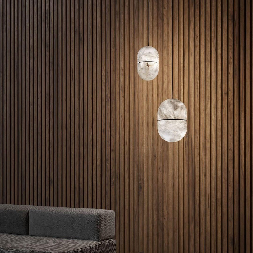 Two Clérachic alabaster pendants against dark vertical timber slats, with the edge of a grey sofa at the bottom of the frame.