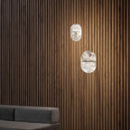 Two Clérachic alabaster pendants against dark vertical timber slats, with the edge of a grey sofa at the bottom of the frame.
