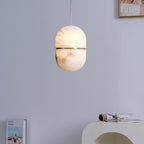 The same Clérachic alabaster pendant lit, its upper half glowing warm, on a lilac wall above a white arched console and a magazine.