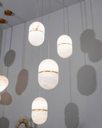 Looking up at four Clérachic alabaster pendants at different heights against a grey wall, their capsule shadows cast behind them.