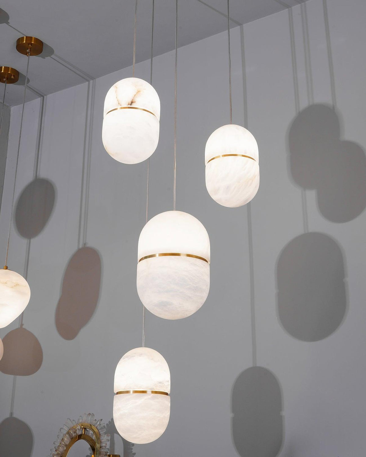 Looking up at four Clérachic alabaster pendants at different heights against a grey wall, their capsule shadows cast behind them.