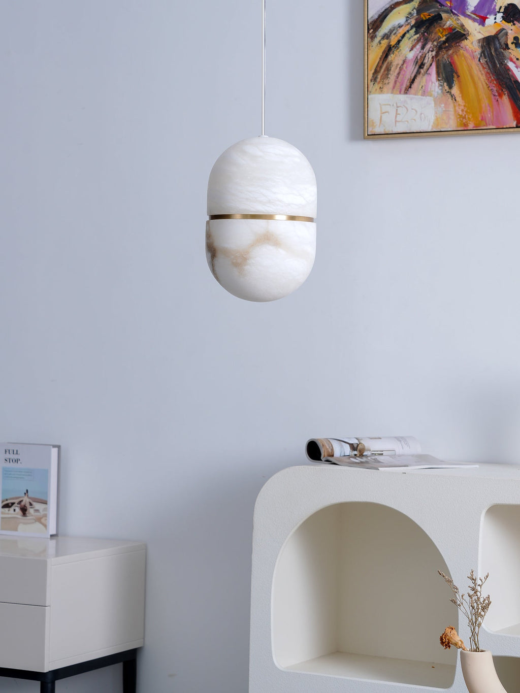 A Clérachic alabaster pendant, unlit, in front of a lilac wall with a corner of a painting and a white arched console.