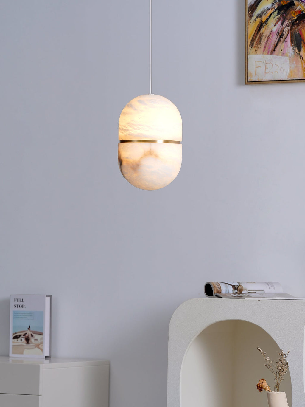 This Clérachic alabaster pendant lit softly, hung beside a painting and above a white console with a stack of books.