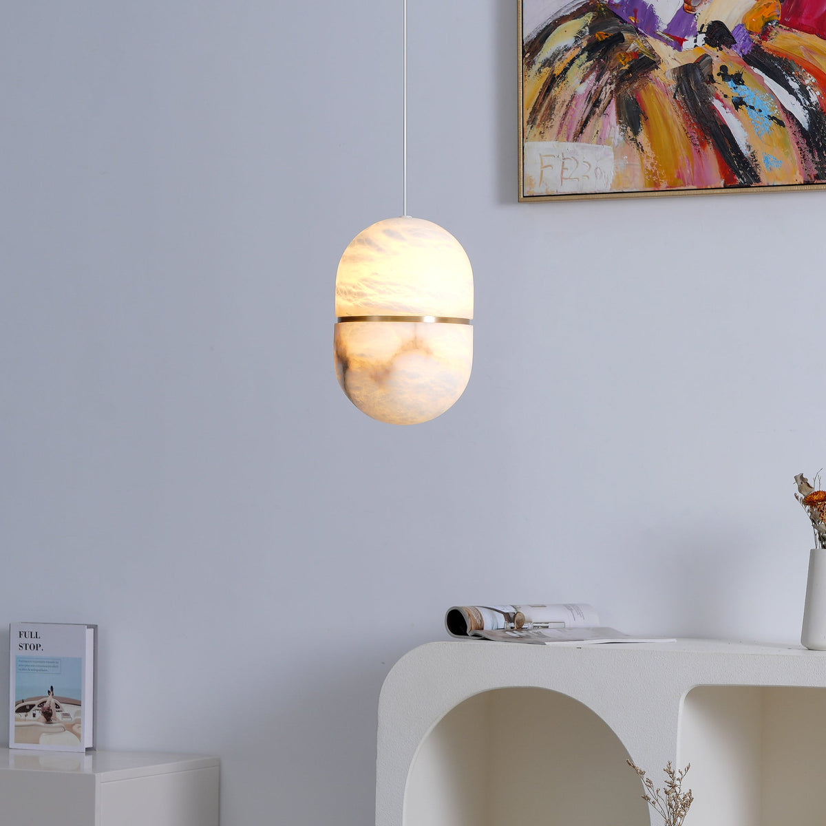 A Clérachic alabaster pendant glowing at the lower half, against a pale lilac wall, with a painting above and a console below.