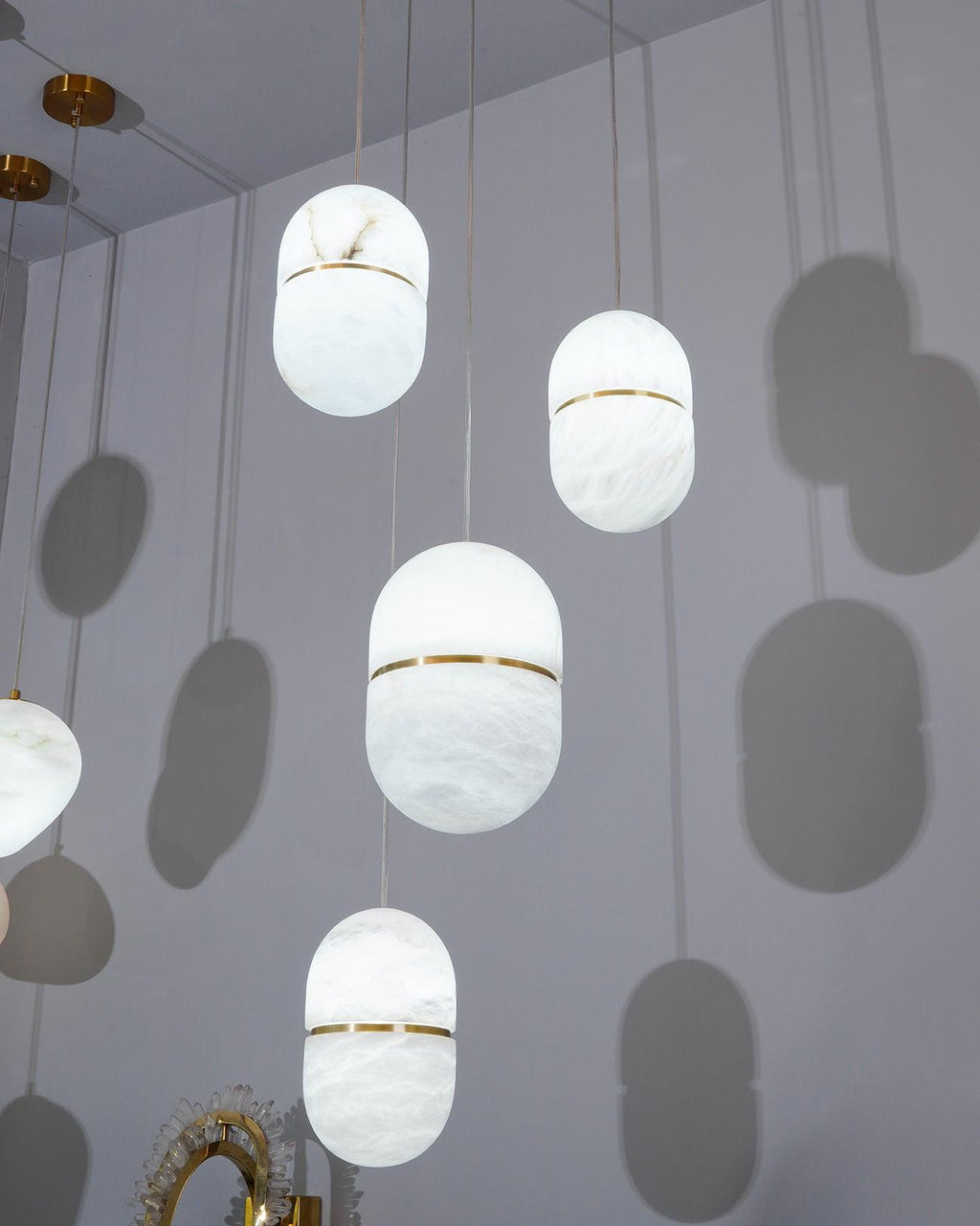Looking up at several Clérachic alabaster pendants in a pale room, each casting a soft capsule-shaped shadow on the wall.