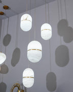 Looking up at several Clérachic alabaster pendants in a pale room, each casting a soft capsule-shaped shadow on the wall.