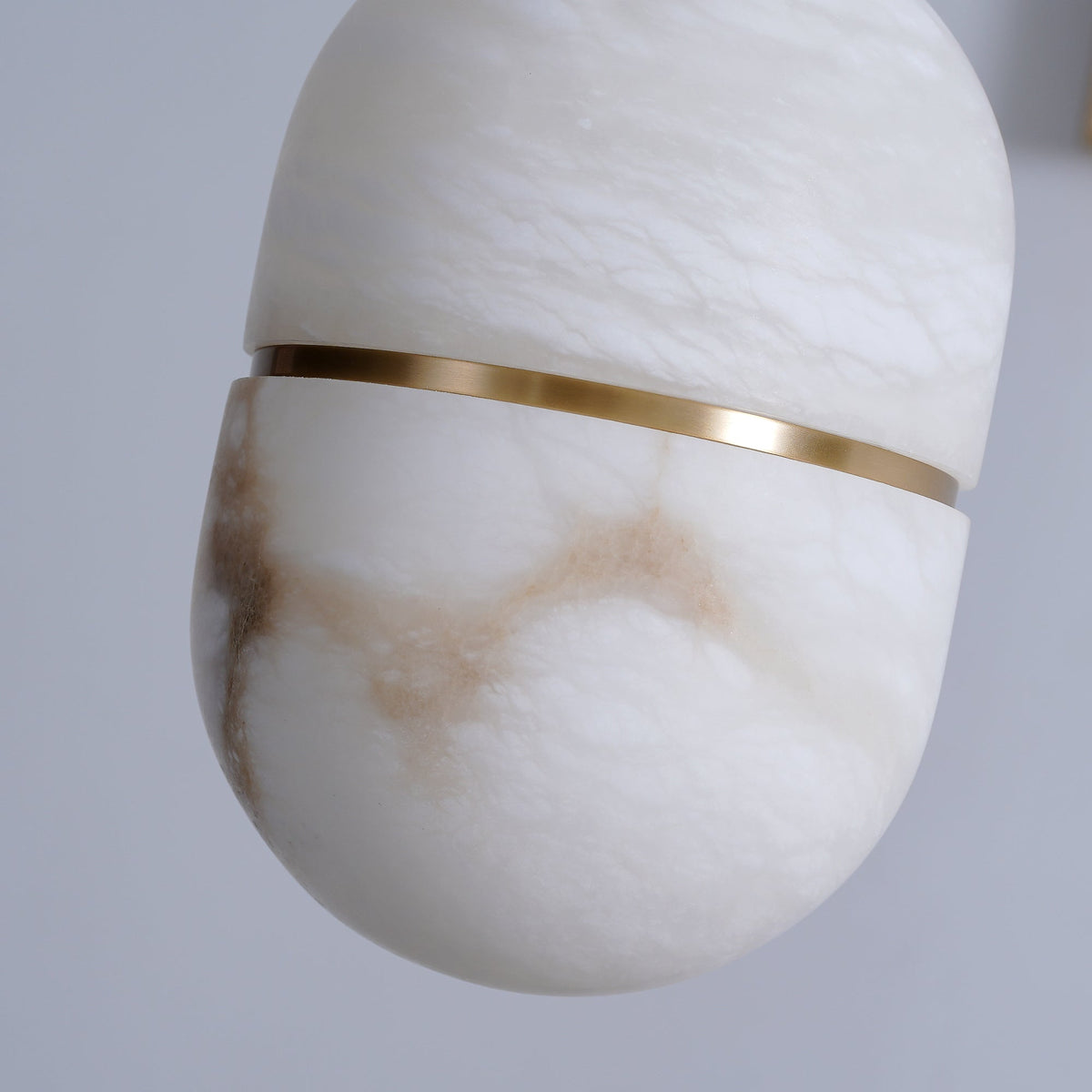 Close view of the veining and the slim gold band on this Clérachic alabaster pendant, with brown streaks through the white stone.