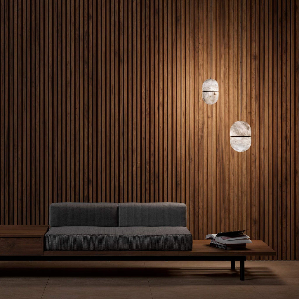 Two small Clérachic alabaster pendants against a timber-slat wall, above a low grey sofa on a wooden bench.