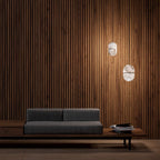 Two small Clérachic alabaster pendants against a timber-slat wall, above a low grey sofa on a wooden bench.