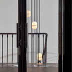Clérachic alabaster pendants hung at different heights beside a black-framed doorway and a stair railing in a pale hall.
