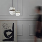 Two small Clérachic alabaster pendants on a pale panelled wall, with a large black-and-white abstract print below.