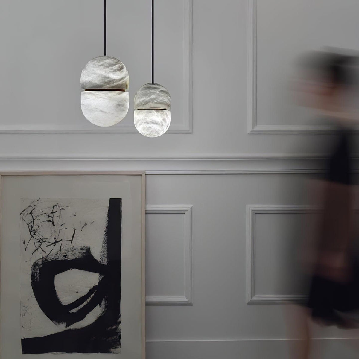 Two small Clérachic alabaster pendants on a pale panelled wall, with a large black-and-white abstract print below.